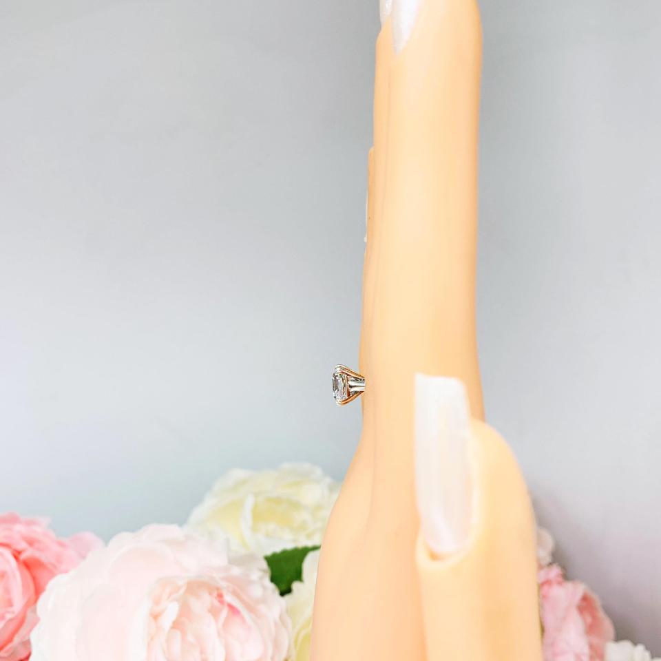 Mannequin hand with long white shimmery nails, displayed against a soft white-gray background with pink and white floral accents. The hand is wearing a sterling silver split-prong cathedral engagement ring set with a colorless old mine cut cubic zirconia.