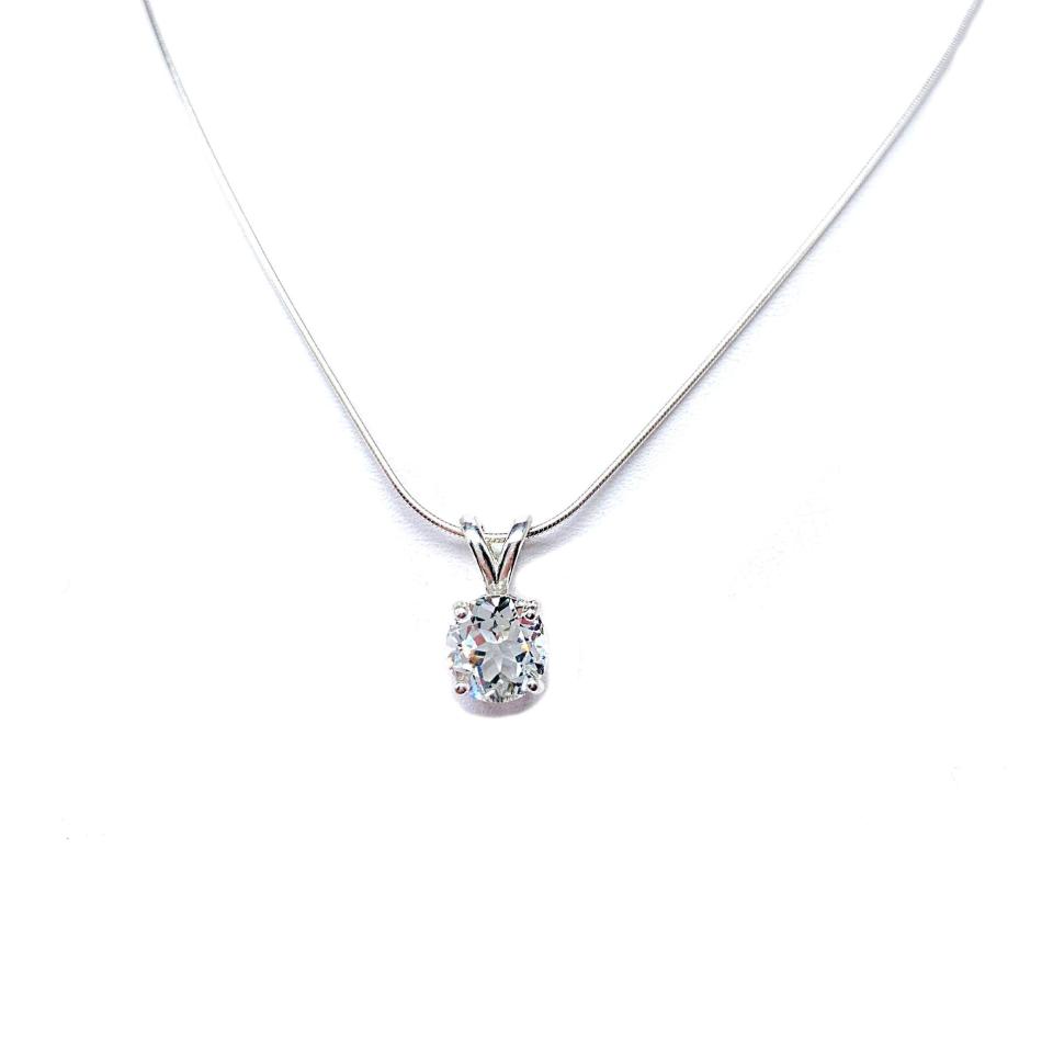 Sterling silver necklace featuring a round-cut white topaz pendant in a four-prong setting, suspended from a delicate silver chain. The natural gemstone is available in six size options and displays brilliant sparkle against a white background.