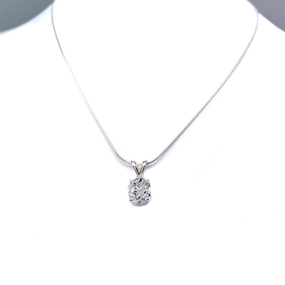 Sterling silver necklace featuring a round-cut white topaz pendant in a four-prong setting, suspended from a delicate silver chain. The natural gemstone is available in six size options and displays brilliant sparkle against a white background.
