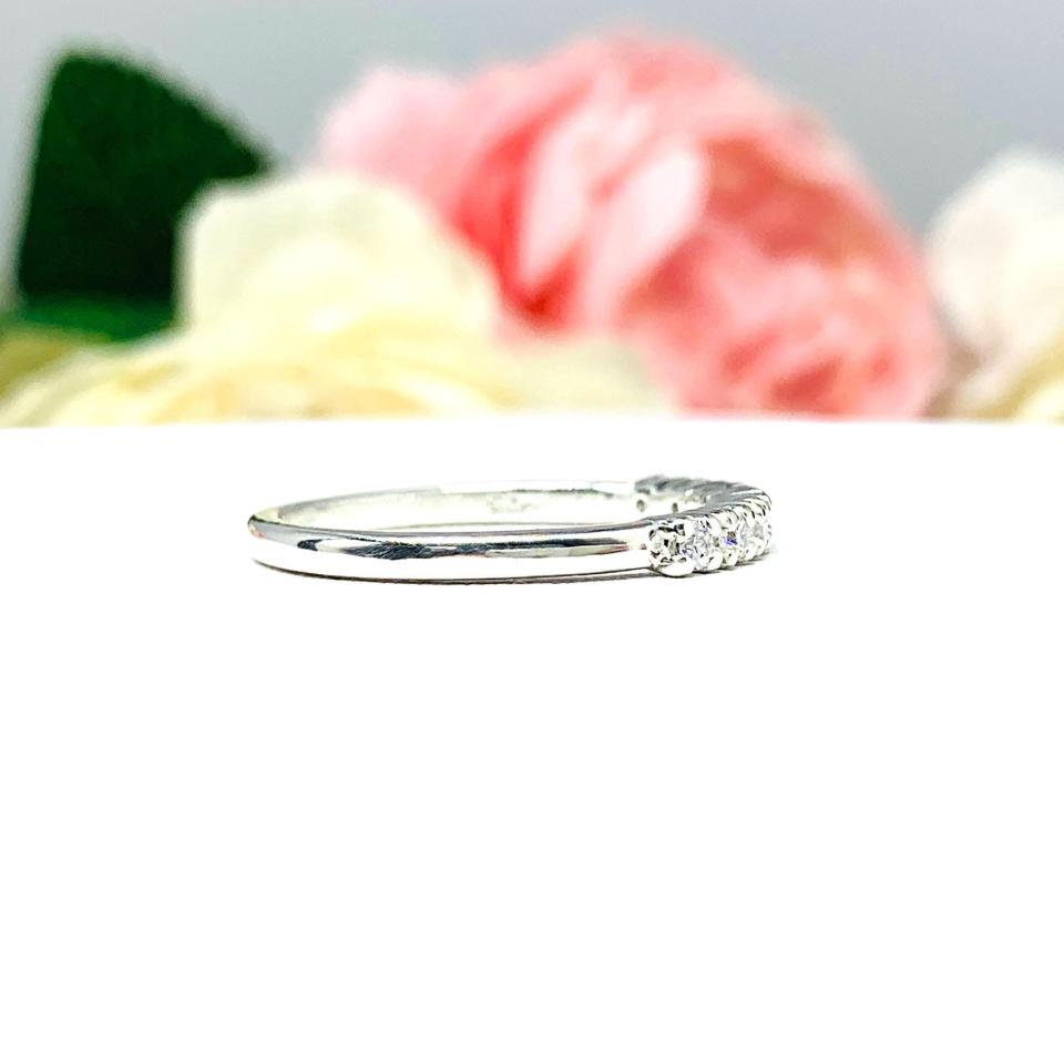 Sterling silver half-eternity, stackable 7-stone wedding band featuring 2mm round precision faceted cubic zirconia stones in prong settings, displayed against a soft floral background.