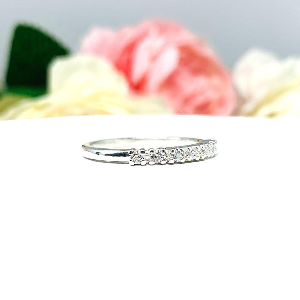 Sterling silver half-eternity, stackable 7-stone wedding band featuring 2mm round precision faceted cubic zirconia stones in prong settings, displayed against a soft floral background.