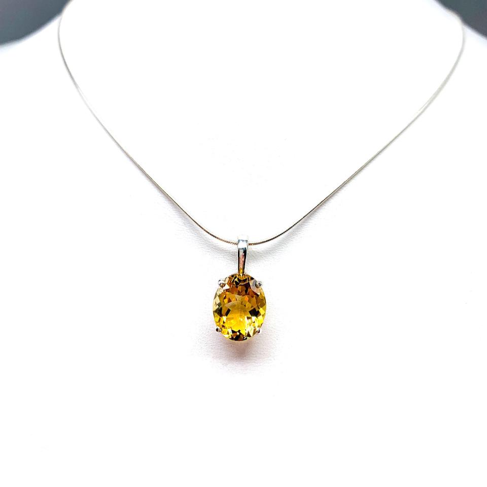 A sterling silver necklace with a pendant featuring a 12x10mm oval-cut, golden citrine gemstone. The necklace is resting against a white background.