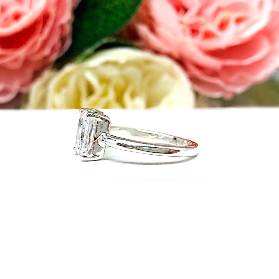 Close‑up of a sterling silver toi et moi ring featuring a an 8x5mm morganite pink color pear‑cut CZ and an 8x6mm colorless radiant-cut cz. Displayed on a white surface with a floral background.