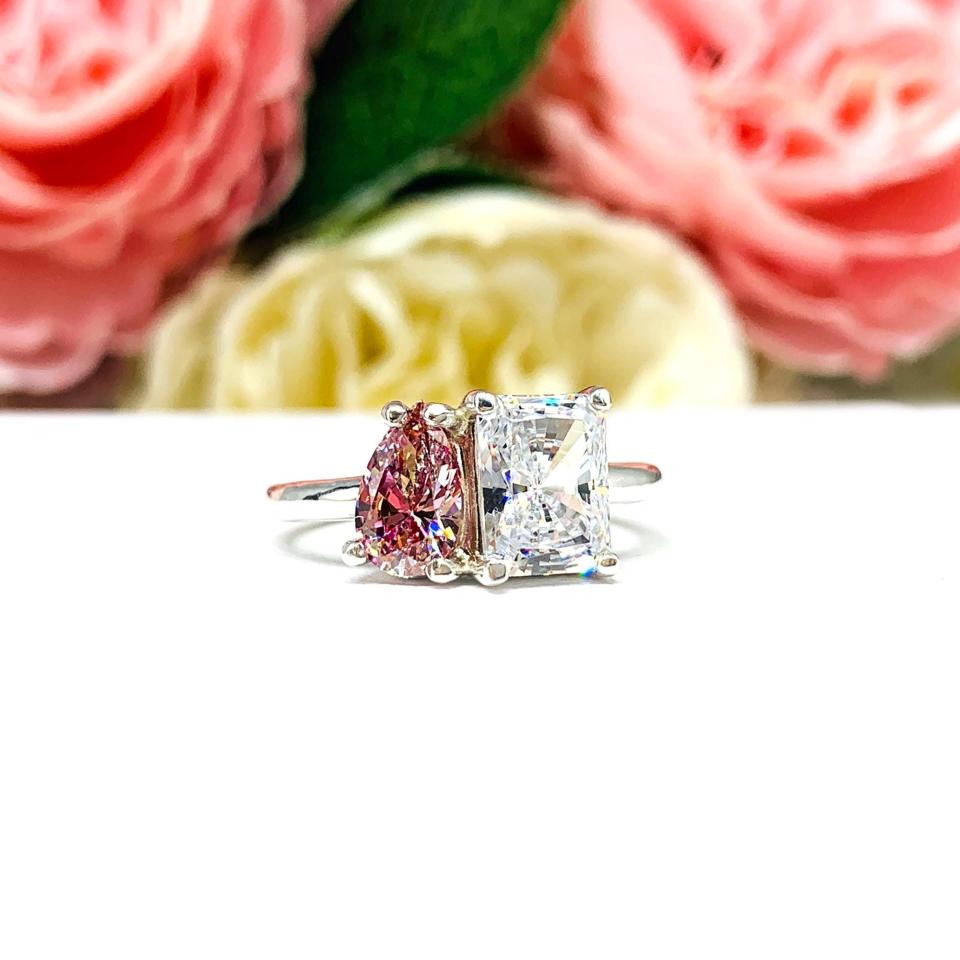 Close‑up of a sterling silver toi et moi ring featuring a an 8x5mm morganite pink color pear‑cut CZ and an 8x6mm colorless radiant-cut cz. Displayed on a white surface with a floral background.