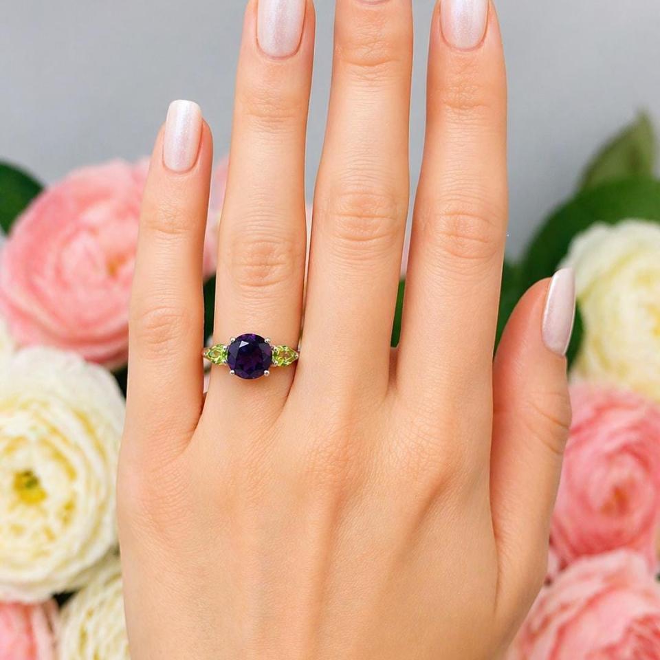 Sterling silver ring featuring a round-cut deep purple African amethyst flanked by two bright green pear-cut Arizona peridots, shown worn on the hand of a woman. Model image for size and styling reference — not a photo of the actual ring