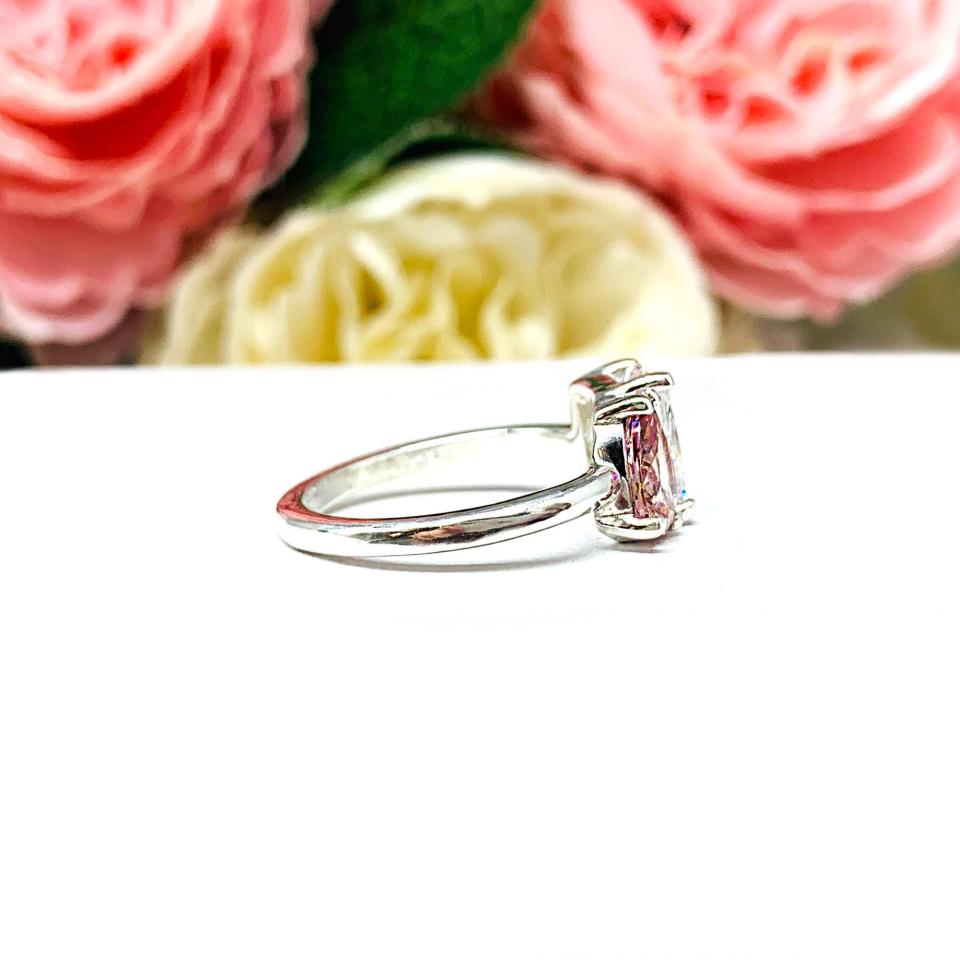 Close‑up of a sterling silver toi et moi ring featuring a an 8x5mm morganite pink color pear‑cut CZ and an 8x6mm colorless radiant-cut cz. Displayed on a white surface with a floral background.