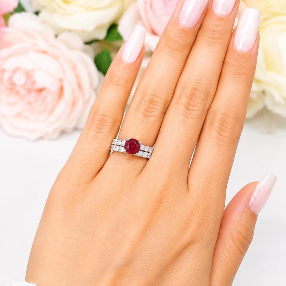 A woman's hand wearing a sterling silver engagement ring featuring a 7mm round lab ruby and 2.5mm round czs on the band. Shown with matching wedding band. Model image for size and styling reference — not a photo of the actual ring.