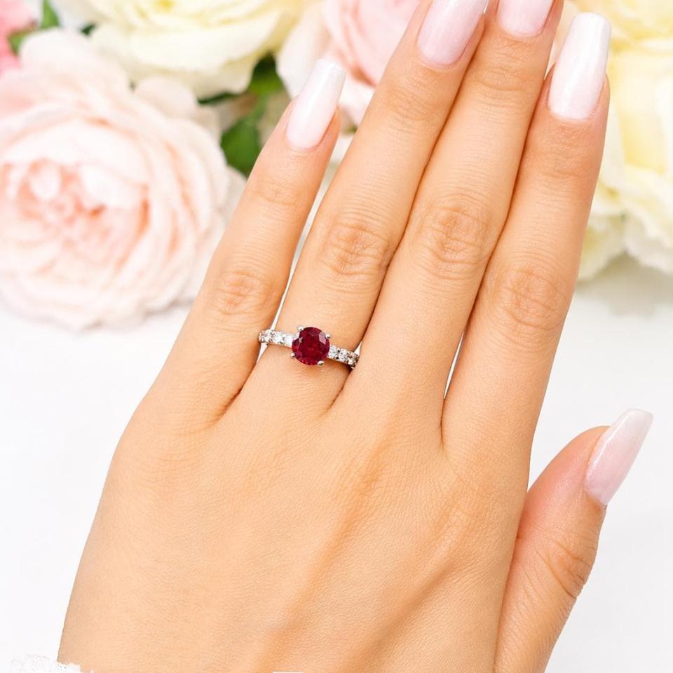 A woman's hand wearing a sterling silver engagement ring featuring a 7mm round lab ruby and 2.5mm round czs on the band. Model image for size and styling reference — not a photo of the actual ring.