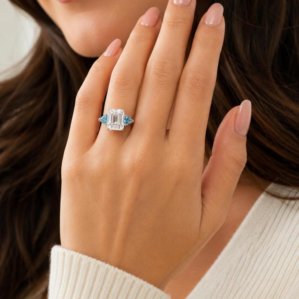 A woman wearing a sterling silver 3-stone ring featuring an 11x9mm lab created white sapphire flanked by two 5mm swiss blue topaz gemstones. Model image for size and styling reference — not a photo of the actual ring.
