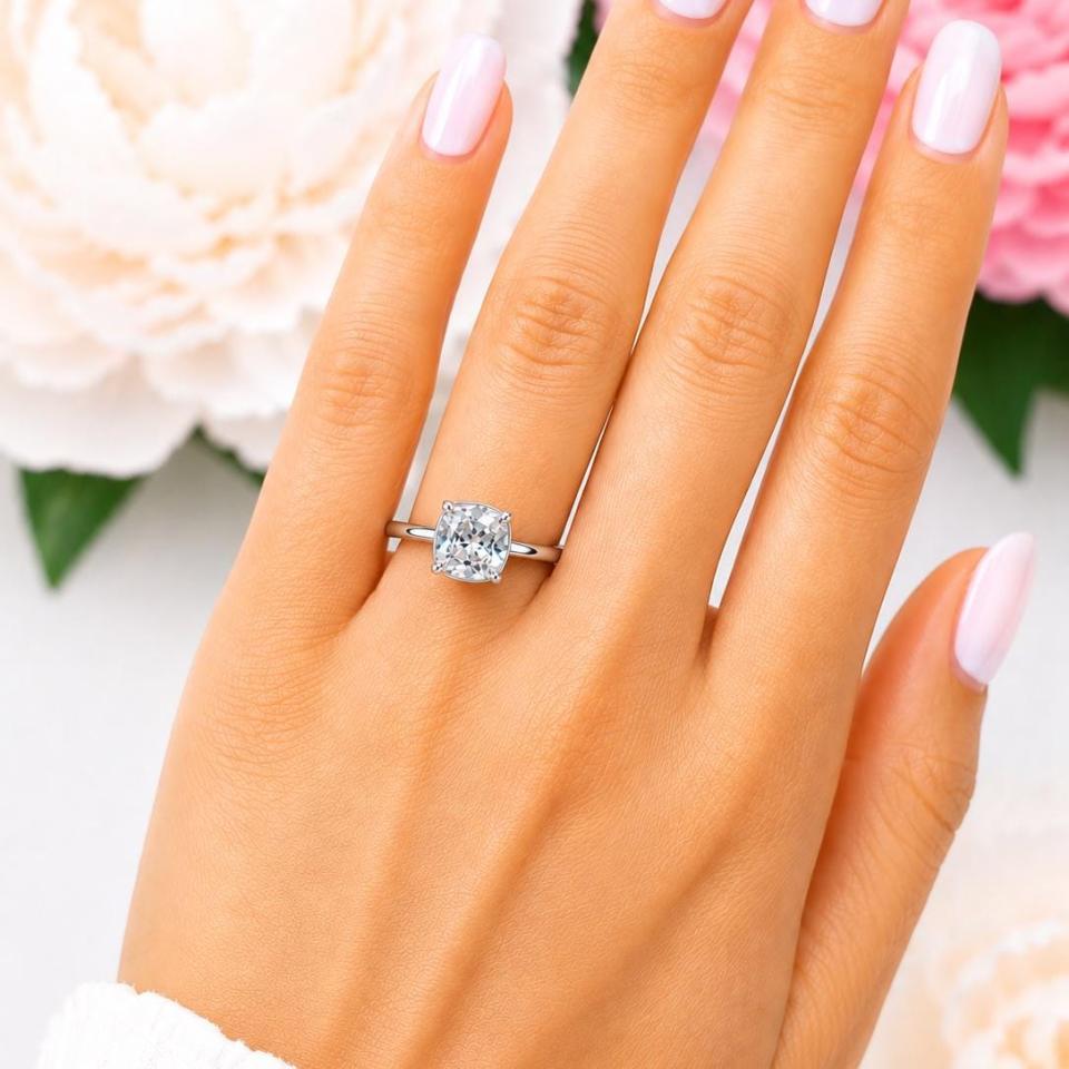 A woman's hand wearing a sterling silver ring with an 8mm cushion-cut lab white sapphire. The stone is set in a bezel prong setting, and the band is rounded and polished. Model image for size and styling reference — not a photo of the actual ring.