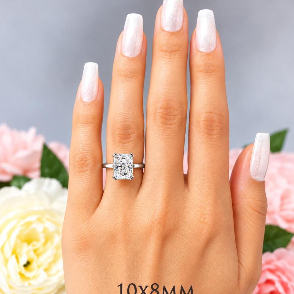 A woman's hand wearing a sterling silver double-prong 10x8mm radiant-cut cubic zirconia solitaire engagement ring. Model image for size and styling reference — not a photo of the actual ring.