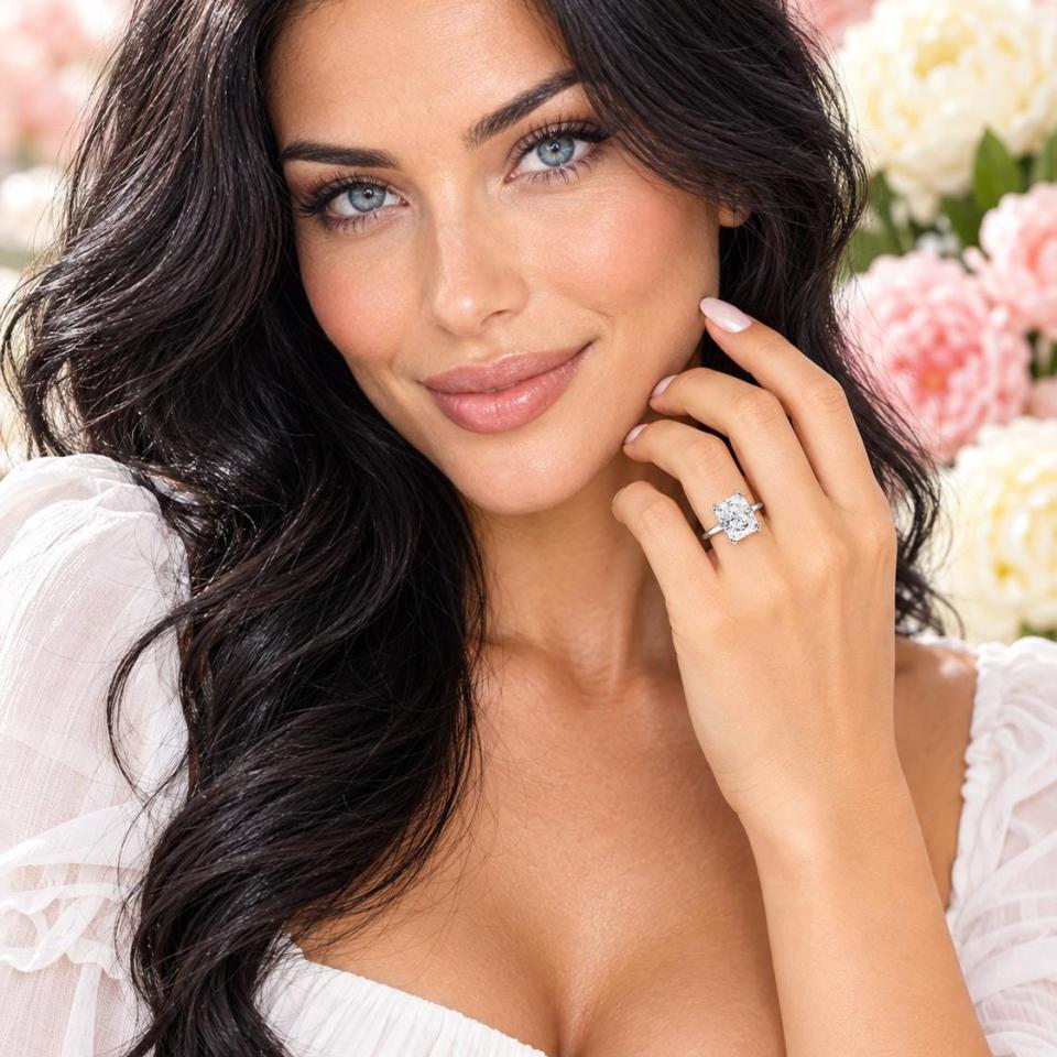 A woman wearing a sterling silver double-prong radiant-cut cubic zirconia solitaire engagement ring. Model image for size and styling reference — not a photo of the actual ring.
